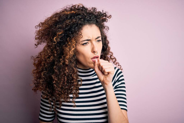 Young beautiful woman with curly hair and piercing wearing casual striped t-shirt feeling unwell and coughing as symptom for cold or bronchitis. Health care concept. - Zdjęcie, obraz