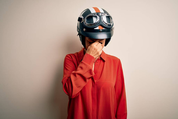 中年のオートバイの女性が疲れ鼻や目をこすり疲れや頭痛を感じ、孤立した白い背景の上にオートバイのヘルメットを着用。ストレスとフラストレーションの概念. - 写真・画像