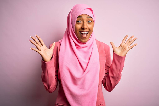 Fiatal afro-amerikai afro nő visel muszlim hidzsáb felett elszigetelt rózsaszín háttér ünnepli őrült és csodálkozott a siker karok felemelt és nyitott szemmel sikoltozó izgatott. Nyertes koncepció - Fotó, kép