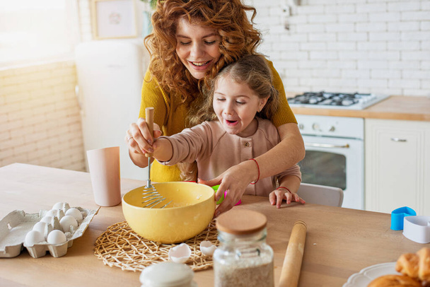 Mother and daughter prepare a cake together in the kitchen - Foto, Imagen