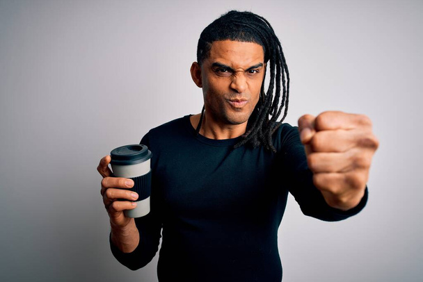 Молодий афроамериканський афро-американський чоловік п'є чашку кави на білому тлі роздратований і розчарований крик з гнівом, божевільний і кричить з піднятою рукою, концепцією гніву
 - Фото, зображення