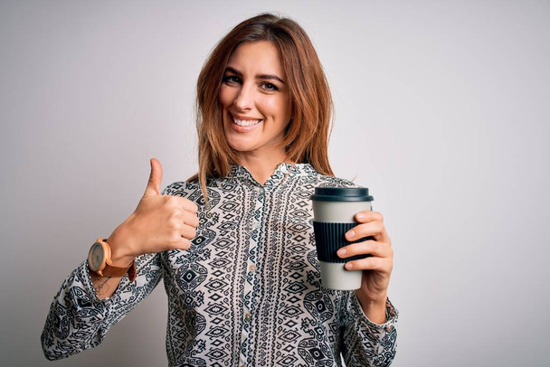Young beautiful brunette woman drinking glass of takeaway coffe over white background happy with big smile doing ok sign, thumb up with fingers, excellent sign - Foto, immagini