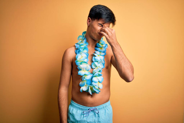 Tatilde mayo ve Hawaii çiçekleri giyerek gezen yakışıklı genç turist yorgun burnu ve gözleri ovuşturup yorgun ve baş ağrısı çekiyor. Stres ve hüsran kavramı. - Fotoğraf, Görsel