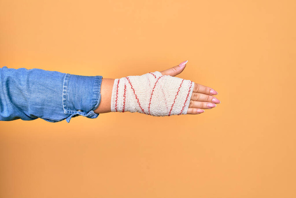 Раненая рука кавказской девушки прикрывается повязкой, жест рукопожатия на изолированном желтом фоне - Фото, изображение