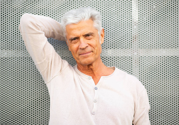 Πορτρέτο όμορφος ηλικιωμένος άνδρας ακουμπά στον τοίχο με το χέρι πίσω από το κεφάλι - Φωτογραφία, εικόνα