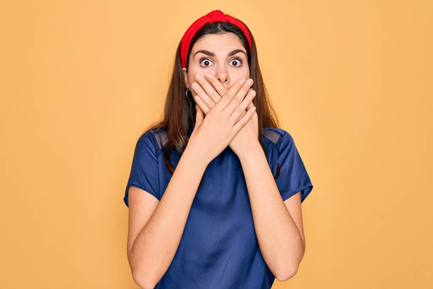 Young beautiful brunette woman wearing red lips over yellow background shocked covering mouth with hands for mistake. Secret concept. - Photo, image