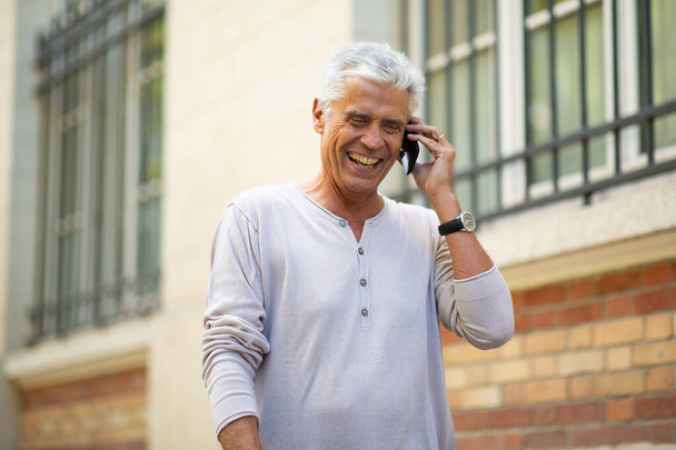 Close up portret starszego człowieka rozmawiając z telefonu komórkowego i śmiejąc się w mieście - Zdjęcie, obraz