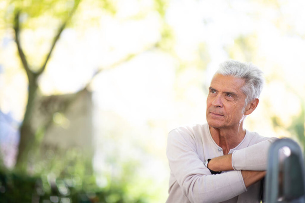 Portrait handsome elderly man sitting on park bench looking away - Photo, Image