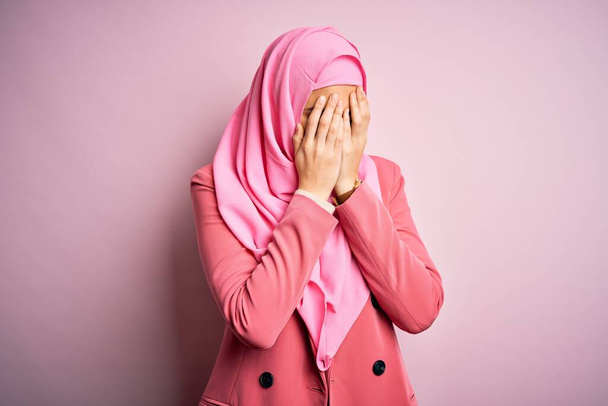 Young beautiful girl wearing muslim hijab standing over isolated pink background with sad expression covering face with hands while crying. Depression concept. - Фото, изображение