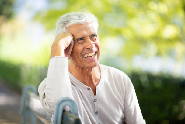 Close up portret knappe oudere man zitten op park bank en glimlachen - Foto, afbeelding