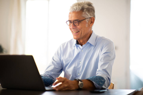 Retrato sonriendo hombre mayor sentado en casa mirando el ordenador portátil
 - Foto, Imagen