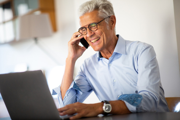 Primer plano retrato sonriente hombre de negocios hablando con el teléfono mientras mira el ordenador portátil
 - Foto, imagen