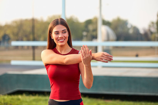 Młoda sportowa kobieta rozciągająca się i ćwicząca w miejskim parku. - Zdjęcie, obraz