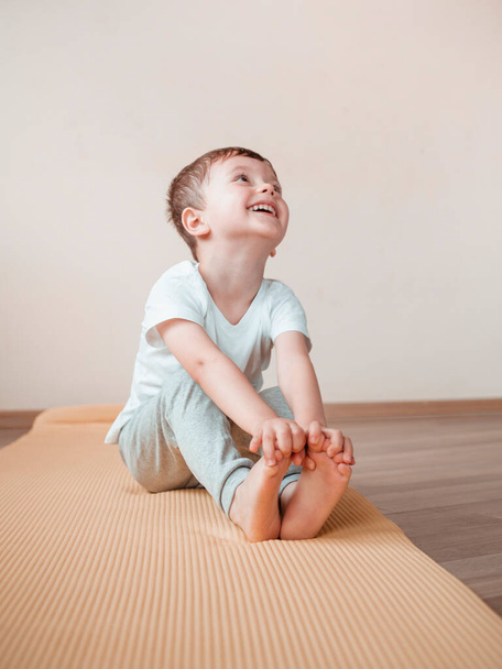 Jóga gyerekeknek otthon. 4 éves fiú nevet, és ül előre kanyarodik jóga gyakorlat - Fotó, kép