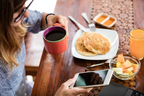 Frau benutzt Laptop und Handy zu Hause beim Frühstück - freiberufliches Konzept. - Foto, Bild