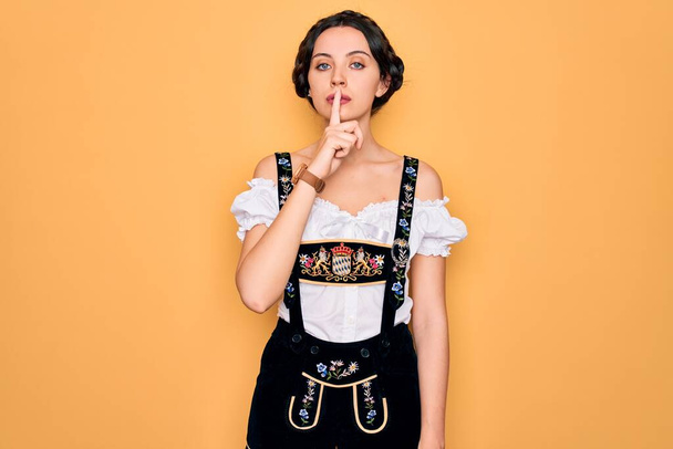 Young beautiful german woman with blue eyes wearing traditional octoberfest dress asking to be quiet with finger on lips. Silence and secret concept. - Фото, зображення