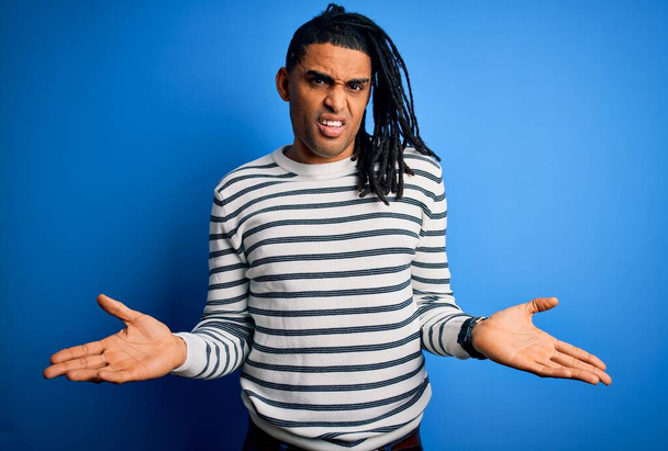 Young handsome african american afro man with dreadlocks wearing casual striped sweater clueless and confused with open arms, no idea concept. - 写真・画像