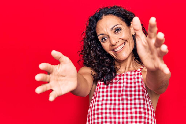 Middle age beautiful woman wearing casual sleeveless t shirt looking at the camera smiling with open arms for hug. cheerful expression embracing happiness.  - Photo, Image