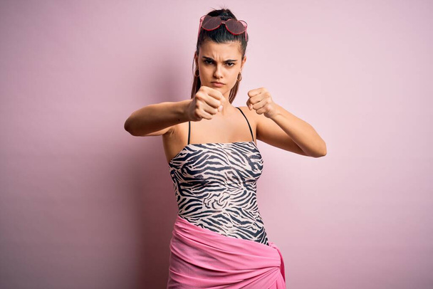 若いです美しいですブルネット女性オン休暇身に着けている水着以上ピンクの背景パンチ拳へ戦い、積極的かつ怒っている攻撃、脅威と暴力 - 写真・画像
