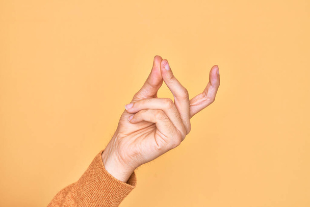 Hand of caucasian young man showing fingers over isolated yellow background snapping fingers for success, easy and click symbol gesture with hand - Фото, изображение