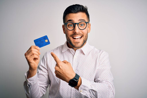 Young business man holding credit card over isolated background very happy pointing with hand and finger - Zdjęcie, obraz