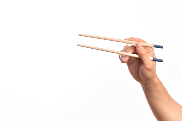 Hand of caucasian young man holding chopsticks over isolated white background - Фото, зображення