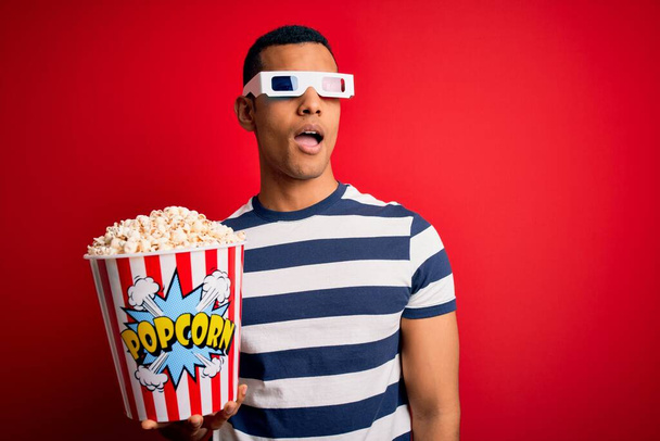 Nuori komea afrikkalainen amerikkalainen mies katselee elokuvaa 3D-laseilla syöden popcorneja, jotka näyttävät uneliailta ja väsyneiltä, väsyneiltä väsymykseen ja krapulaan, laiskoilta silmiltä aamulla.. - Valokuva, kuva