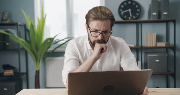 Focused man in eyewear using laptop for work at office - Materiał filmowy, wideo
