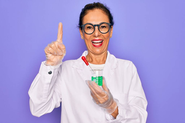 Középkorú vezető tudós nő visel laboratóriumi kabát gazdaság kutatási teszt cső meglepett egy ötlet vagy kérdés mutogató ujjal boldog arc, első számú - Fotó, kép