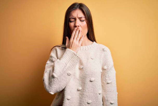 Young beautiful woman with blue eyes wearing casual sweater standing over yellow background bored yawning tired covering mouth with hand. Restless and sleepiness. - Fotó, kép