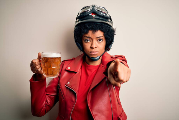 Νεαρή Αφρο-Αμερικανίδα μοτοσυκλετίστρια με σγουρά μαλλιά, βαζάκι μπύρας που δείχνει με το δάχτυλο την κάμερα και σε σένα, ζώδιο χεριού, θετική και σίγουρη χειρονομία από μπροστά - Φωτογραφία, εικόνα