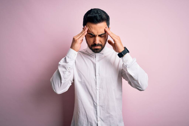 Young handsome man with beard wearing casual shirt standing over pink background with hand on head for pain in head because stress. Suffering migraine. - Фото, изображение