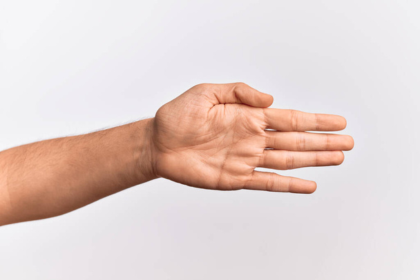 Hand of caucasian young man showing fingers over isolated white background stretching and reaching with open hand for handshake, showing palm - Photo, Image
