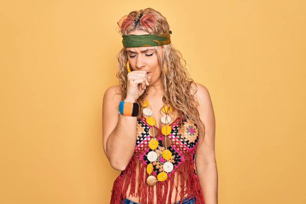 Beautiful blonde hippie woman wearing sunglasses and accessories over yellow background feeling unwell and coughing as symptom for cold or bronchitis. Health care concept. - Foto, afbeelding