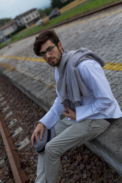 beautiful boy sitting on the train platform on the tracks with glasses. High quality photo - Photo, Image