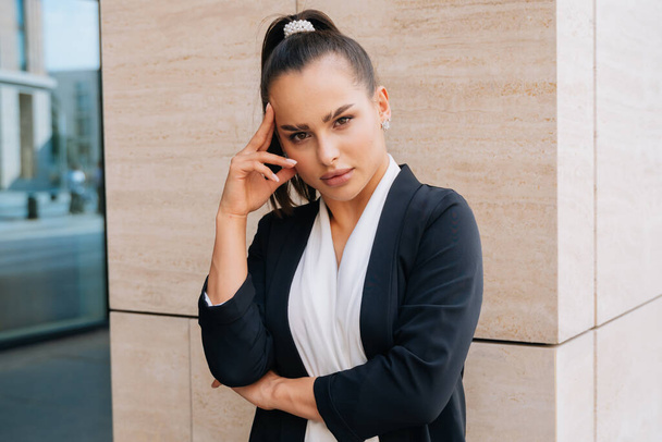A brooding stylish girl looks to the side in a business suit. Average plan against the background of the business center. - Фото, изображение