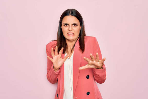 Young beautiful brunette businesswoman wearing elegant jacket over isolated pink background disgusted expression, displeased and fearful doing disgust face because aversion reaction. - Photo, Image