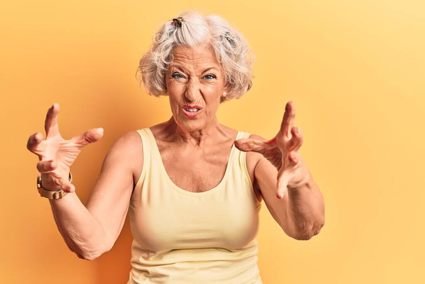 Ηλικιωμένη γκριζομάλλα γυναίκα που φοράει καθημερινά ρούχα φωνάζοντας απογοητευμένη από οργή, με τα χέρια να προσπαθούν να στραγγαλίσουν, φωνάζοντας τρελά  - Φωτογραφία, εικόνα