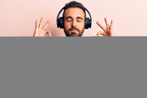 ヘッドフォンを使用して音楽を聴いている若いヒスパニック系の男性は、指で瞑想のジェスチャーを行う閉じて目でリラックスして笑顔。ヨガのコンセプト.  - 写真・画像