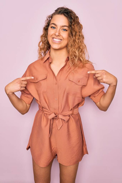 Young beautiful woman with blue eyes wearing casual summer dress over pink background looking confident with smile on face, pointing oneself with fingers proud and happy. - Photo, image