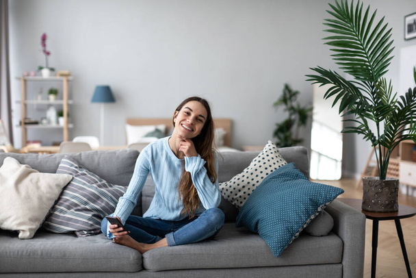 Smiling woman using mobile on the sofa at home. Online chat with friends. - Foto, Imagem