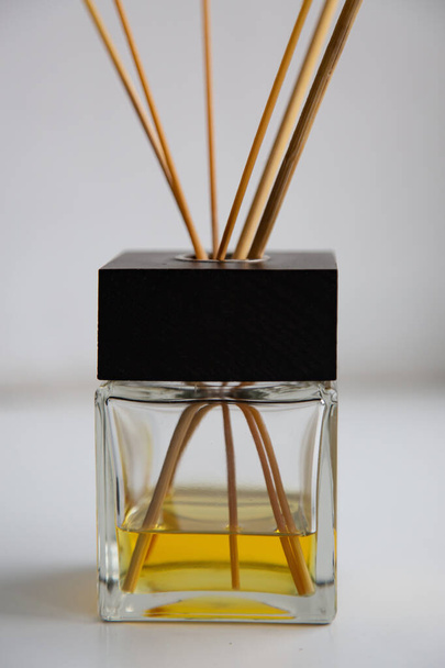 close-up glass diffuser with a black cap, wooden sticks and yellow aromatic oil. white wall in the background. selective focus - 写真・画像