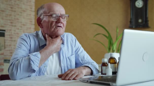 old modern man pensioner in glasses for vision consults a doctor online by video link on a laptop shows pills and drugs - Кадры, видео