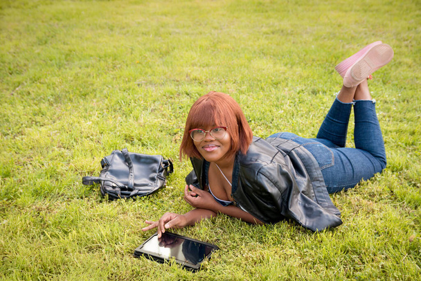 Černá mladá dívka ležící v parku na trávě. Dívka tráví čas v karanténě venku. - Fotografie, Obrázek