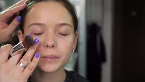 Make-up umělec aplikuje základ krém na obličej s prsty dívky v salonu - Záběry, video