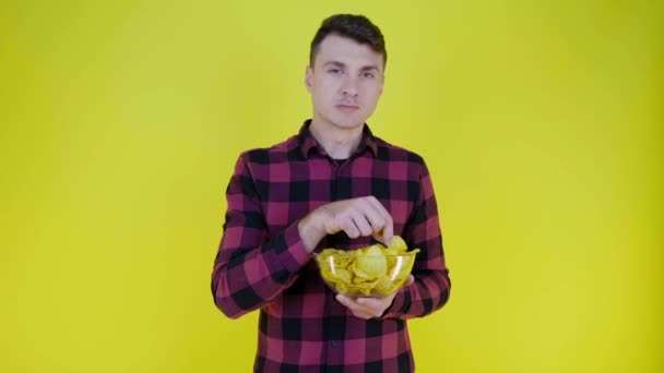 Homme en chemise à carreaux rose mange des croustilles avec bol en verre sur fond jaune - Séquence, vidéo
