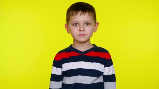 Μικρό αγόρι κοιτάζει την κάμερα σε ένα κίτρινο φόντο με χώρο αντίγραφο - Πλάνα, βίντεο