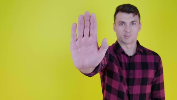 Homem levanta a mão, mostra palma para a câmera e diz parar em um fundo amarelo
 - Filmagem, Vídeo
