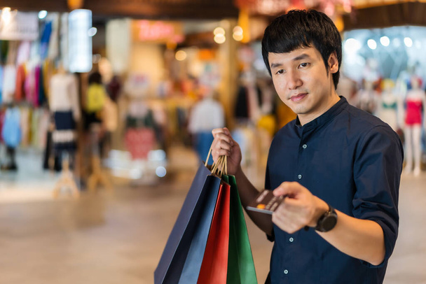 young asian man wearing medical mask and holding a credit card at shopping mall  - Fotografie, Obrázek