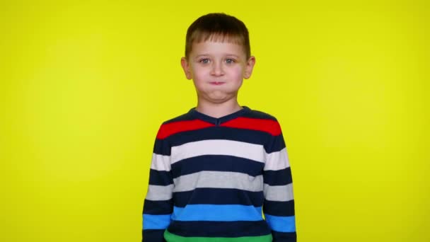 Confused child boy in a colorful sweater on a yellow background with copy space - Footage, Video